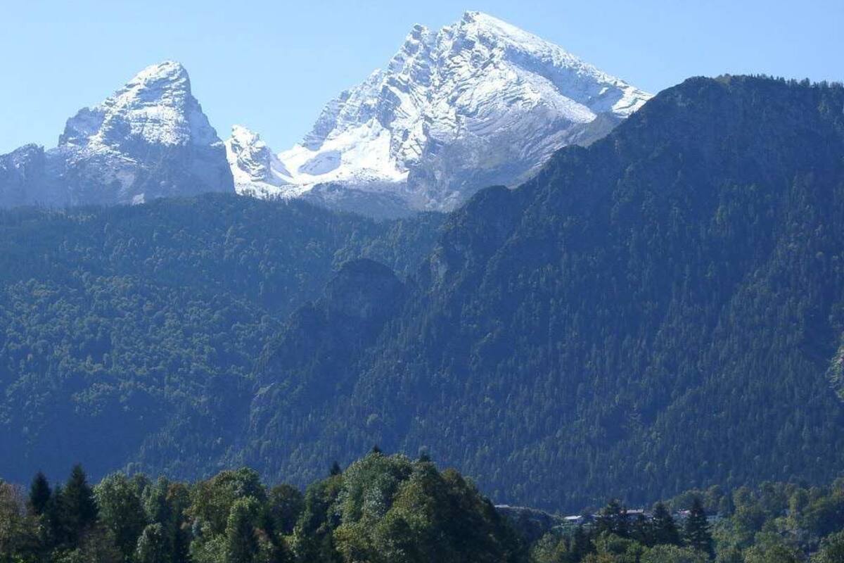 Eine Berglandschaft mit schneebedeckten Gipfeln und dichtem Wald.