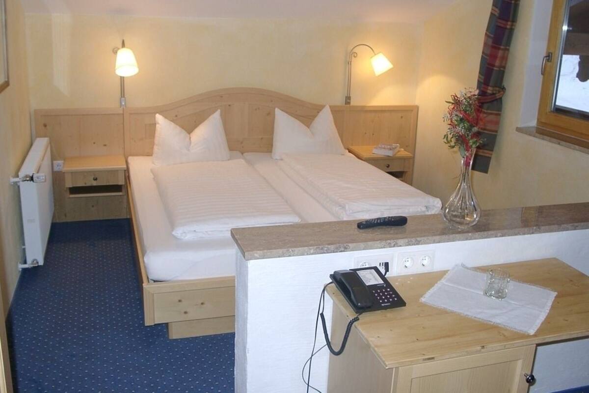 Ein Hotelzimmer mit Doppelbett, Nachttischlampen, einem Schreibtisch mit Telefon und einem Fenster mit Vorhängen.