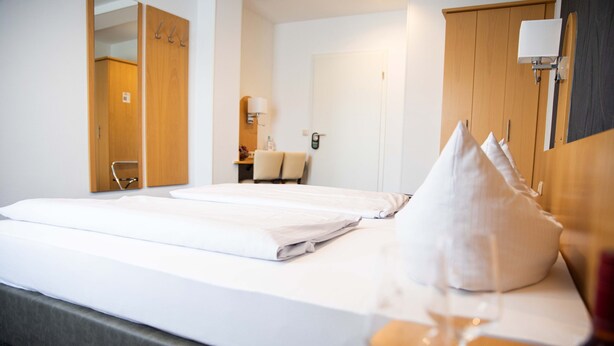 Une chambre d’hôtel avec deux lits, une armoire en bois, un bureau avec une chaise, un miroir et une table de chevet avec un verre à vin.