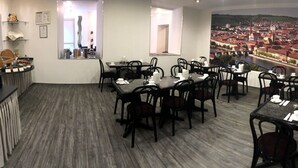 Un espace repas avec plusieurs tables et chaises, un coin cuisine avec un buffet, et une grande fenêtre donnant sur un panorama urbain.