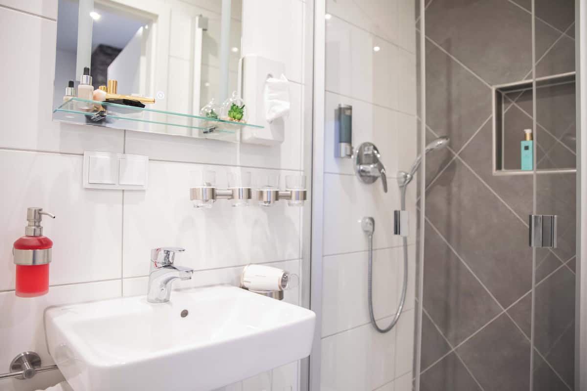 Casa de banho moderna com uma sanita branca, uma prateleira de vidro com produtos de higiene pessoal, um espelho e zona de duche com porta de vidro.