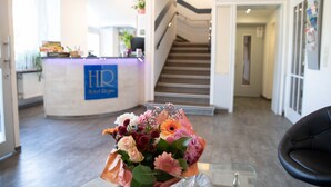 Un espace d’accueil d’hôtel comprenant un comptoir de réception, un escalier et un arrangement floral posé sur une table en verre.