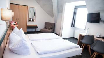 Habitación de hotel con cama, escritorio, silla, televisor, armario y ventana.
