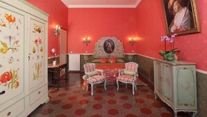 A room with a red and white color scheme, featuring a large cabinet with floral designs, two chairs, a table, and a wall-mounted painting. - Residenza Horti Luculliani (Rome)