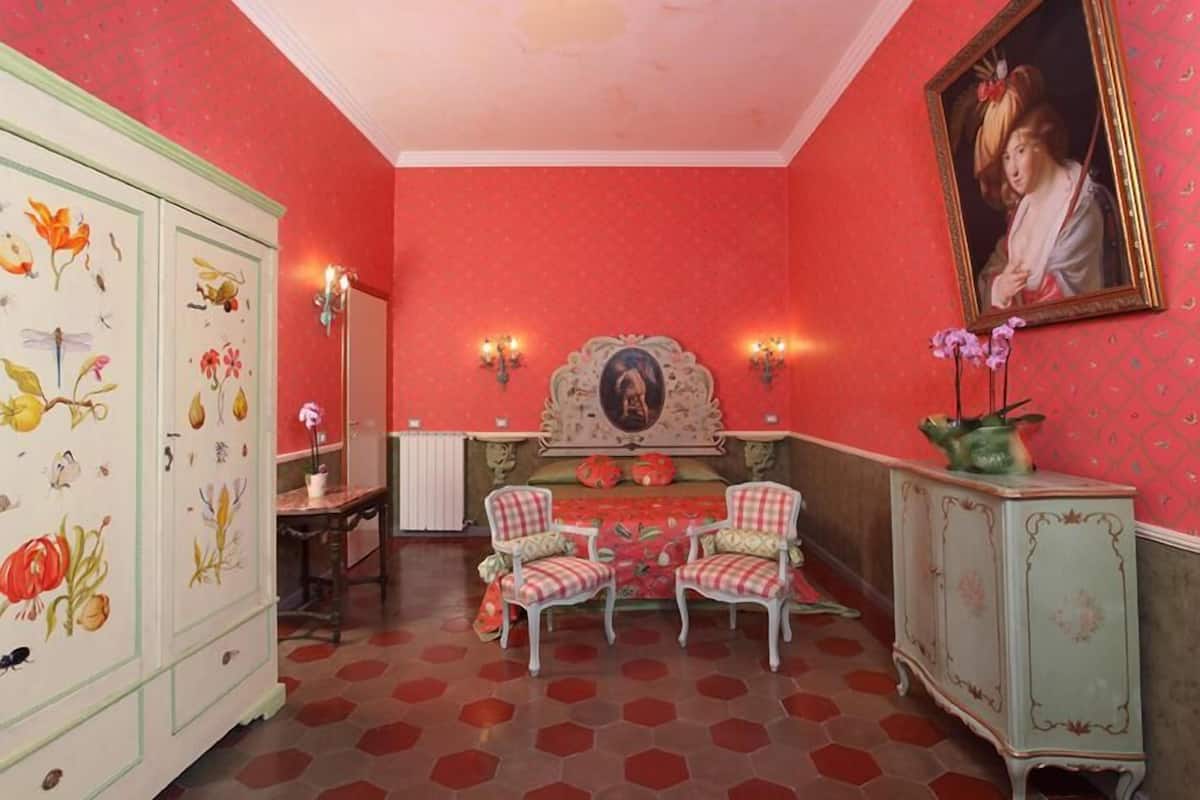 A room with a red and white color scheme, featuring a large cabinet with floral designs, two chairs, a table, and a wall-mounted painting.