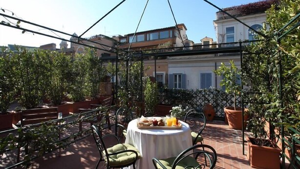 A terrace with a table set for breakfast, surrounded by potted plants and outdoor furniture. - Residenza Horti Luculliani (Rome)
