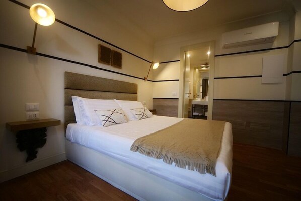 A bedroom with a bed, bedside table, wall-mounted lamp, and an air conditioning unit. - Residenza Horti Luculliani (Rome)