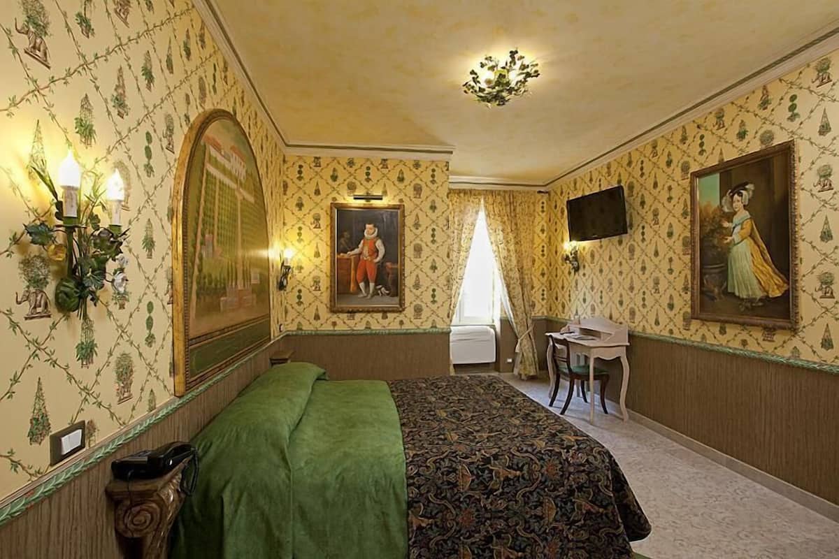 A room with a bed, a desk, a chair, a television, and a chandelier.