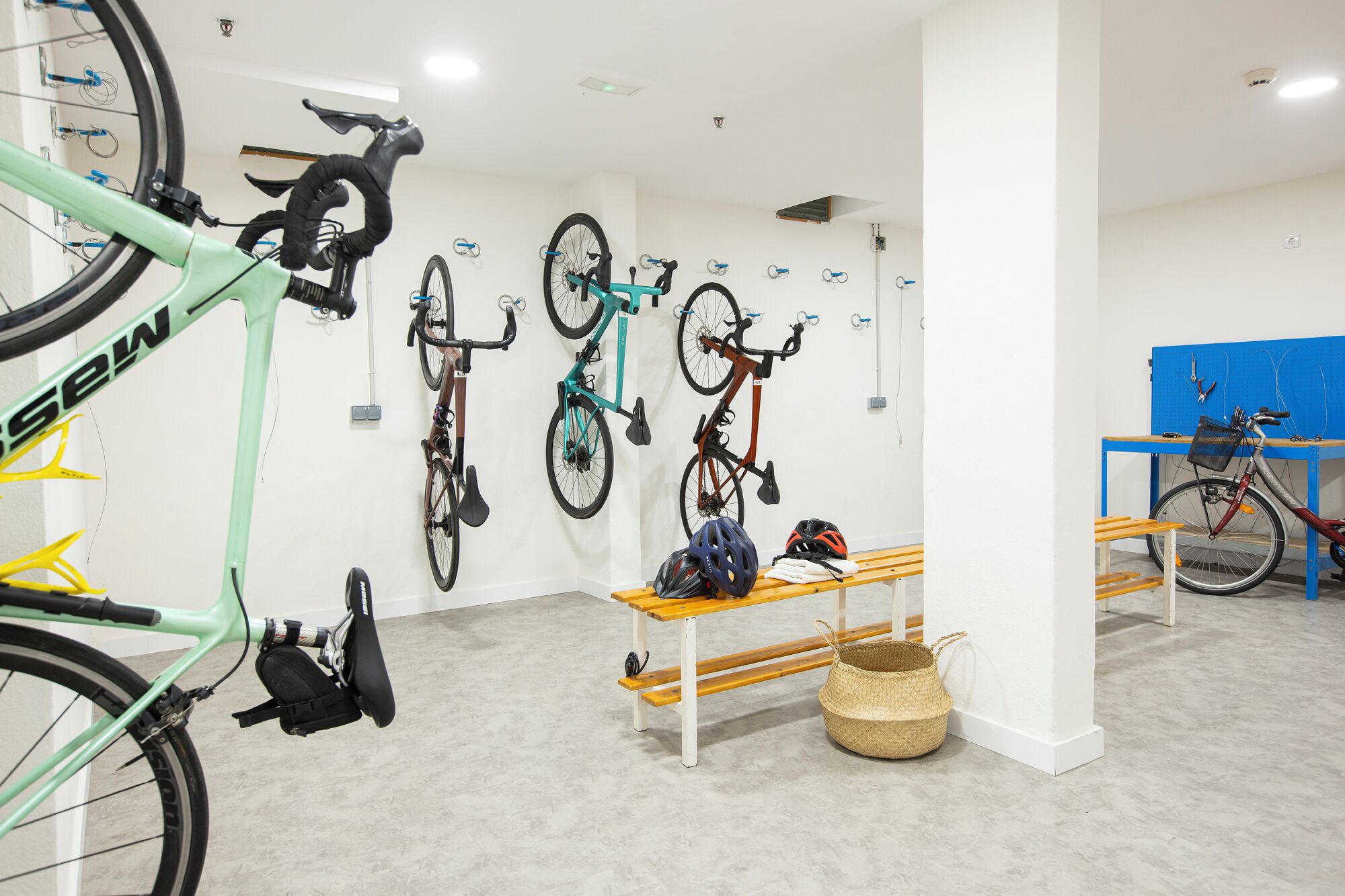 A bicycle storage area with multiple bikes, a wooden bench, and a basket.
