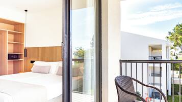 A hotel room with a bed, a wicker chair, and a balcony with a view of the outside.