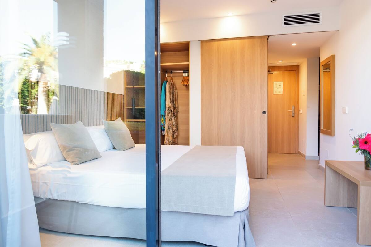 A modern hotel room with a large bed, a wooden wardrobe, and a bathroom visible through an open door.