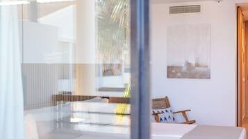 Una habitación de hotel moderna con una cama, una pequeña zona de estar con una silla y cojines, un ventanal grande y una obra de arte colgada en la pared.