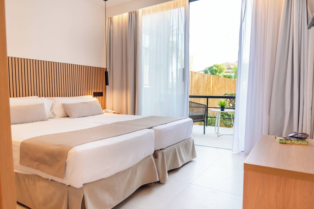 A hotel room with a large bed, a desk, and a balcony with a table and chairs.