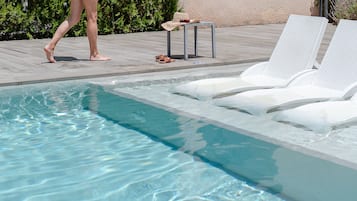 Una piscina al aire libre, sombrillas, sillones reclinables de piscina