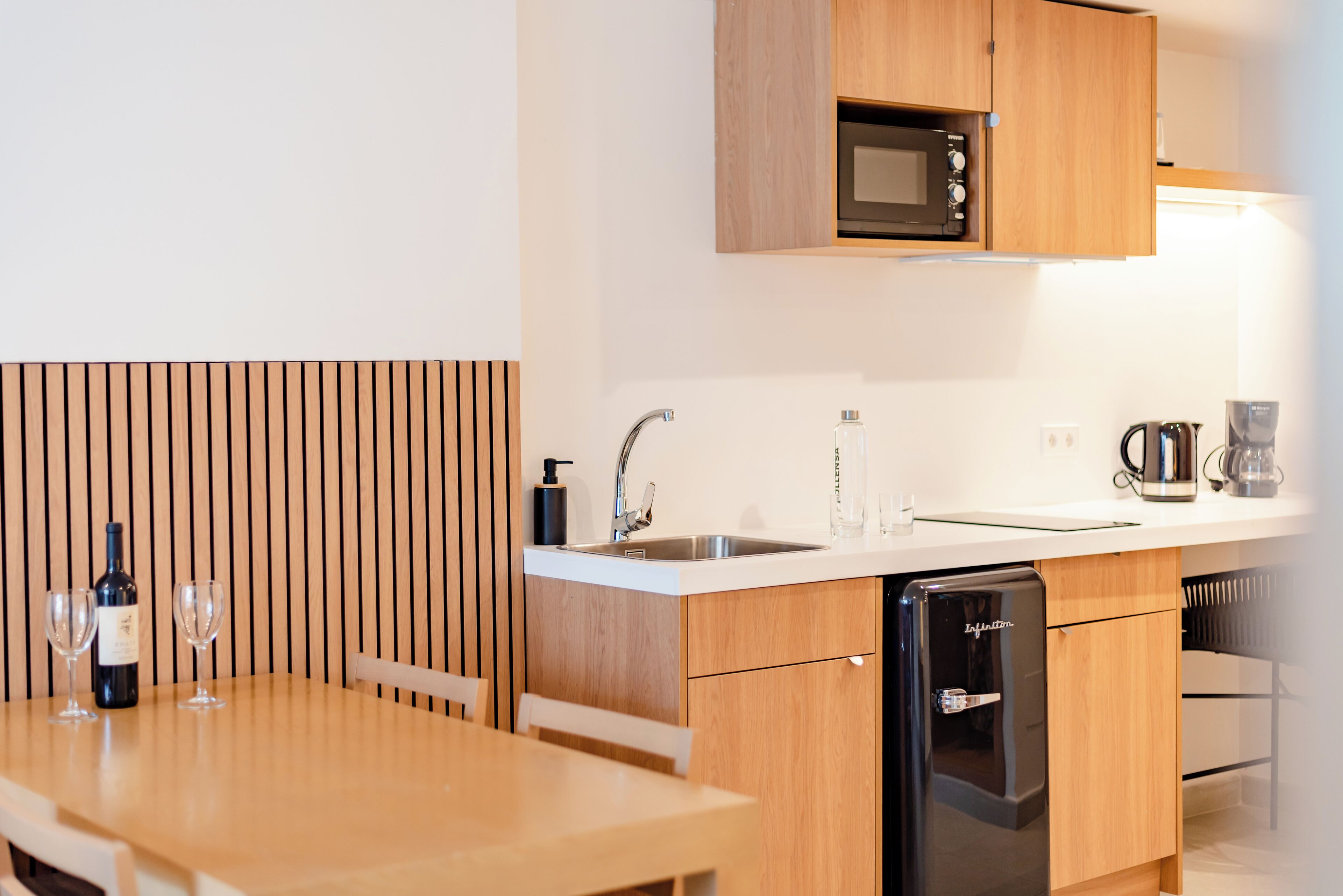 Een kleine keuken met houten kastjes, een ingebouwde magnetron, een spoelbak en een vaatwasser.