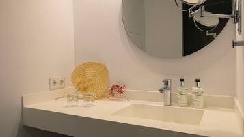 Un baño con un lavamanos blanco, un espejo redondo y tres botellas de jabón corporal.