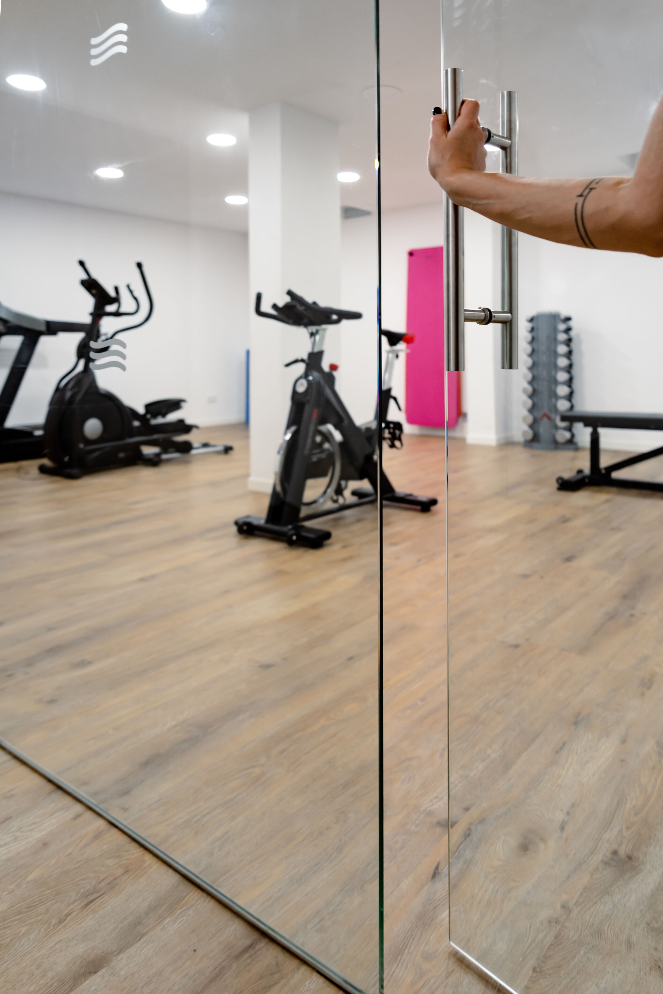 Una palestra con attrezzature per esercizi, pavimento in legno e una parete divisoria in vetro.