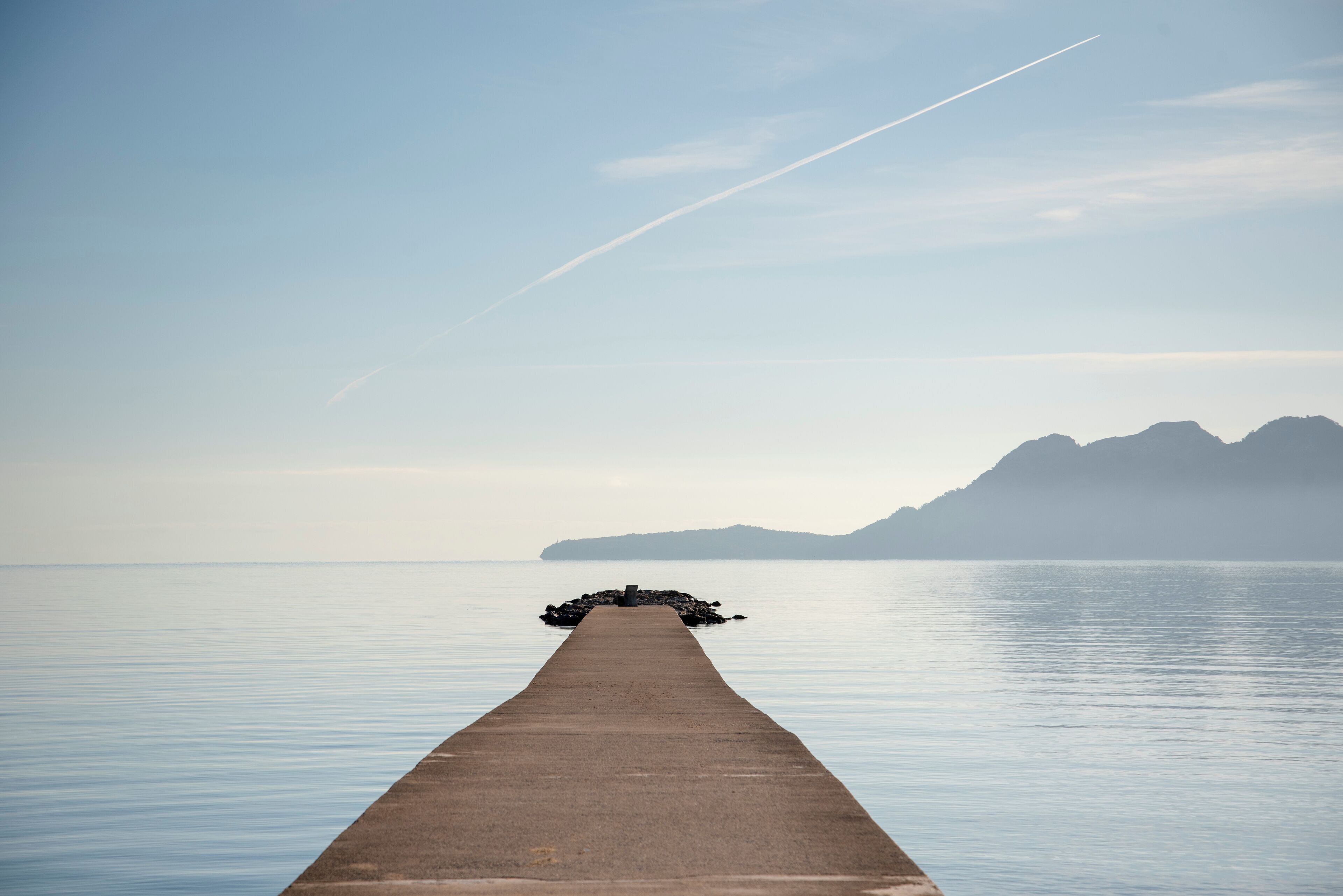 Un muelle de hormigón largo que se adentra en aguas tranquilas, con una montaña al fondo.