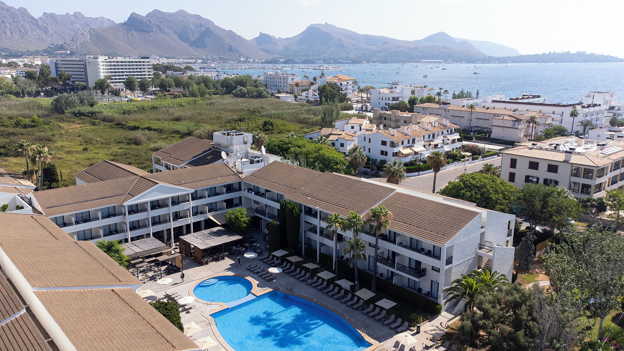 Un hotel con piscina, varios balcones y vistas al mar y a las montañas.