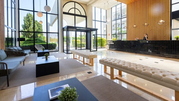A spacious lobby with a reception desk, seating area, and large windows offering views of greenery.