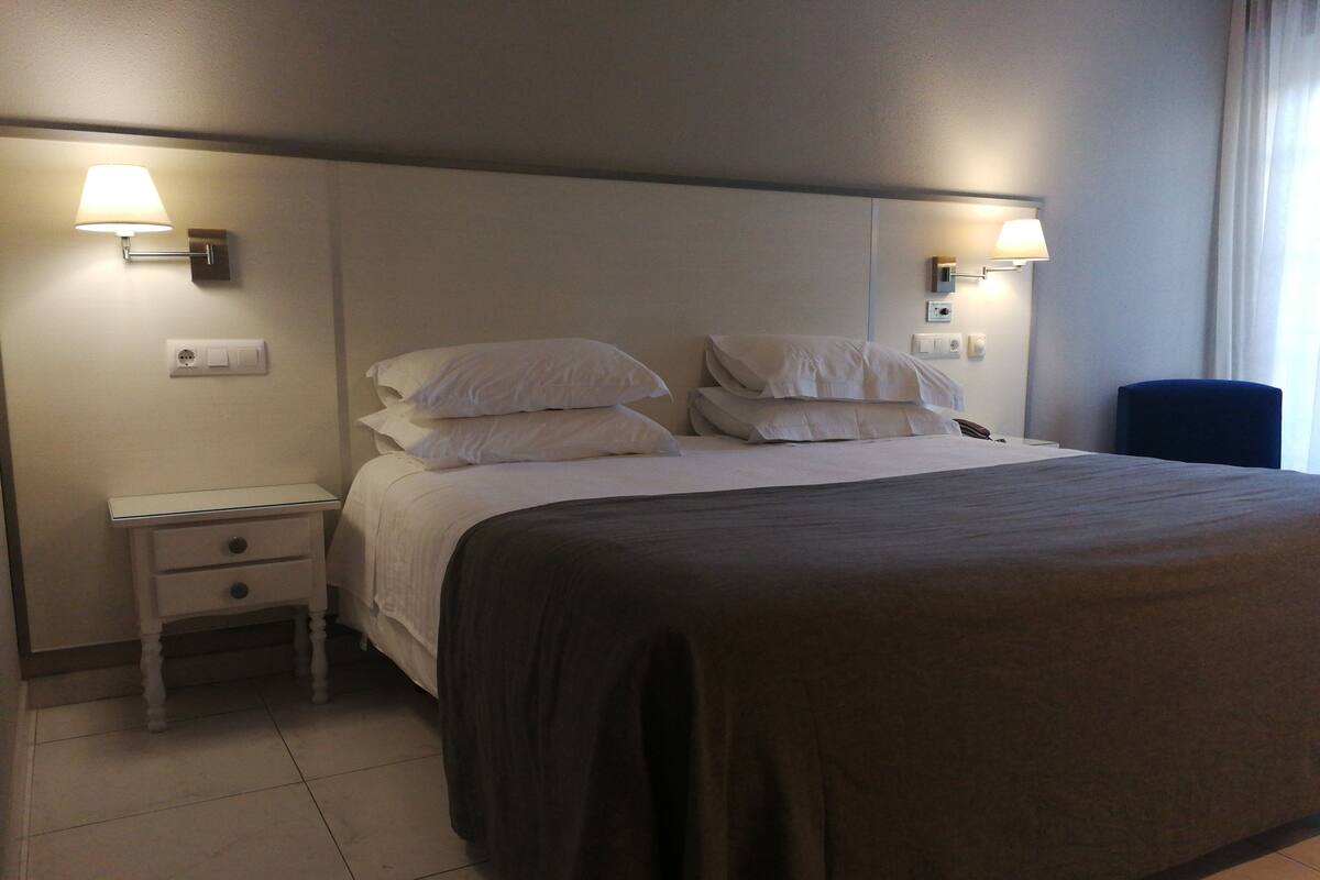 A neatly made bed with a dark-colored bedspread, two bedside tables with lamps, and a blue chair in a hotel room.