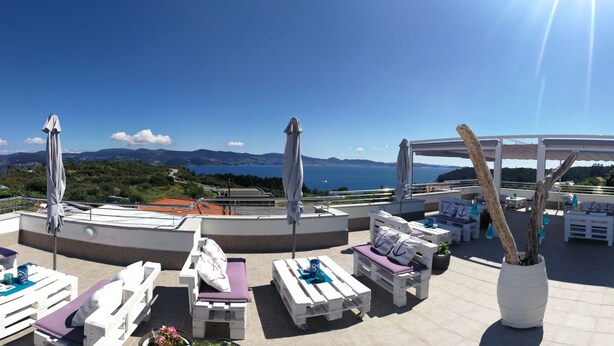 Una terraza en la azotea con mobiliario blanco, una pérgola y vistas al mar y a las montañas.