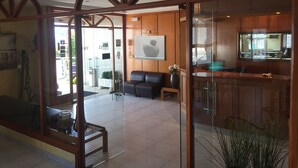 Zona de recepción con un separador de vidrio, mostrador de madera y un área de descanso con sofá y sillones.