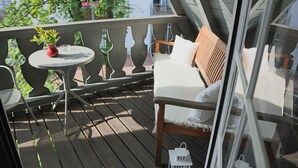 Una terraza de madera con una mesa blanca, un jarrón rojo y una silla blanca con cojín.