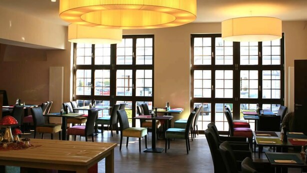 A restaurant with multiple tables and chairs, large windows, and hanging lamps. - Hotel Thiesmann (Muelheim an der Ruhr)