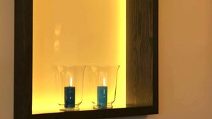 A mirror with a yellowish light and two clear glass vases with blue candles. - Hotel Thiesmann (Muelheim an der Ruhr)