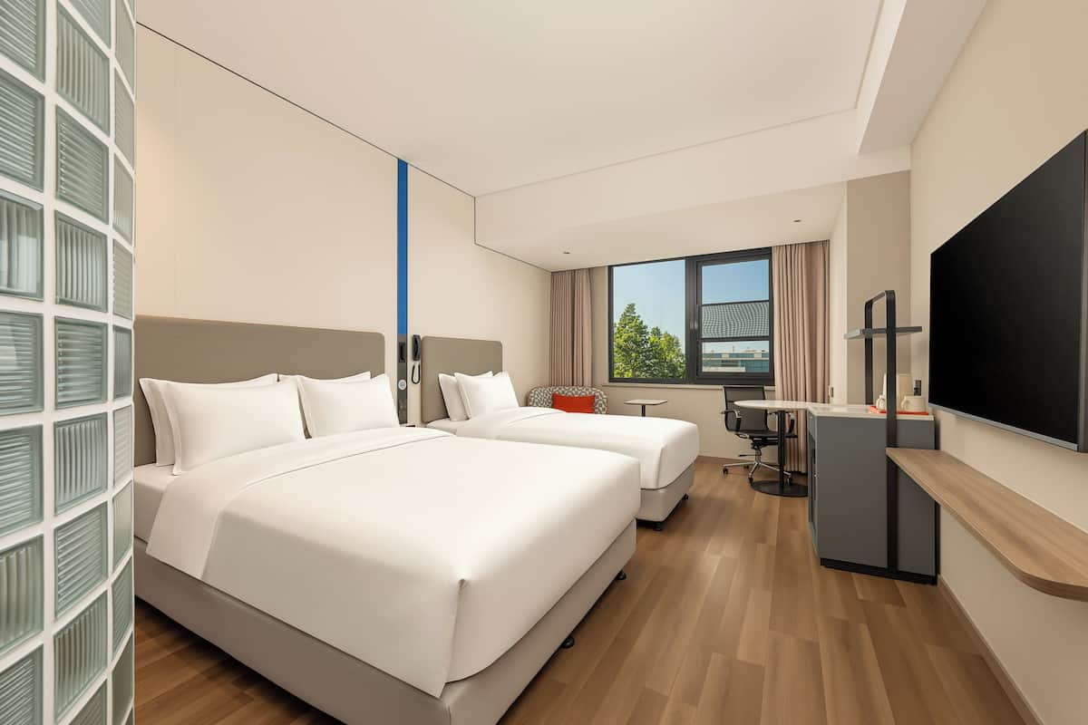 Ein Hotelzimmer mit zwei Betten, einem Schreibtisch, einem Fernseher und einem Fenster mit Blick.