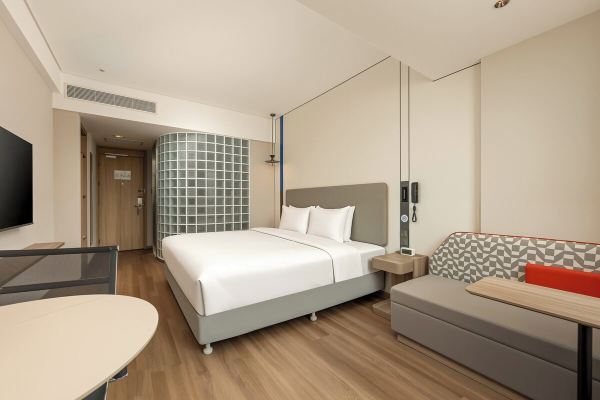 A hotel room with a bed, a desk, a seating area, and a TV.