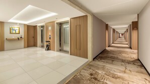 Un couloir d’hôtel avec un sol à carreaux, des lambris en bois et une vue dégagée sur le fond du couloir.