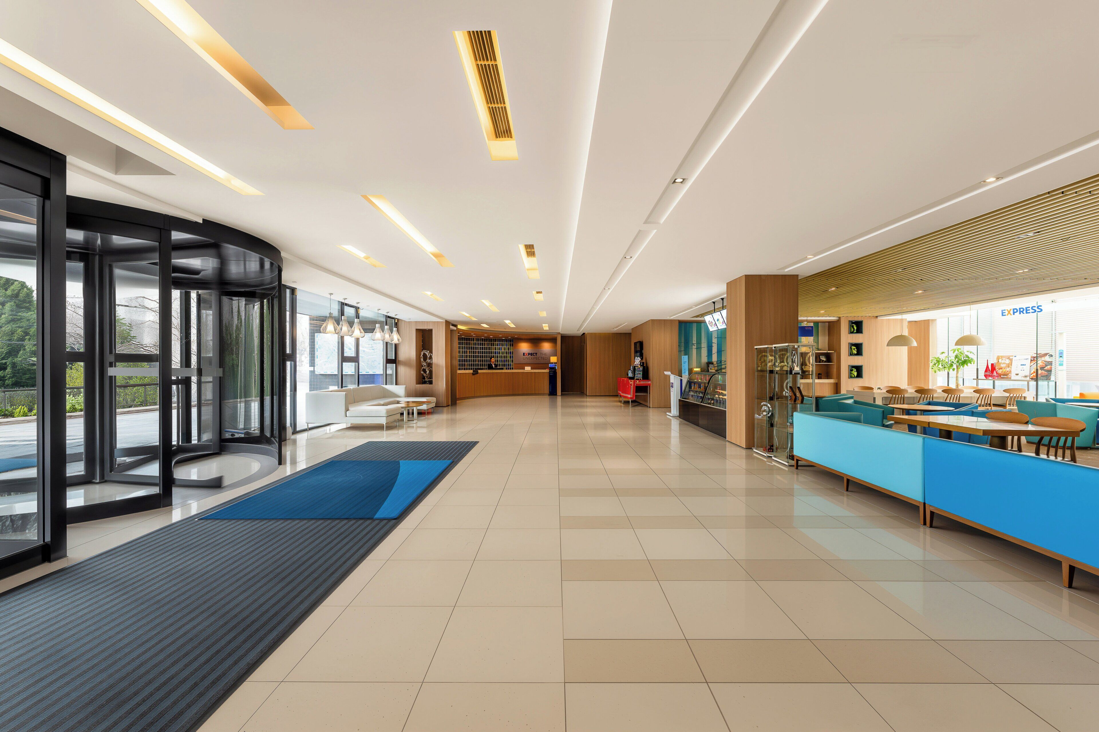 A modern hotel lobby with a reception desk, seating area, and a glass entrance.