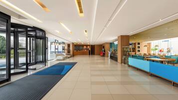A modern hotel lobby with a reception desk, seating area, and a glass entrance.