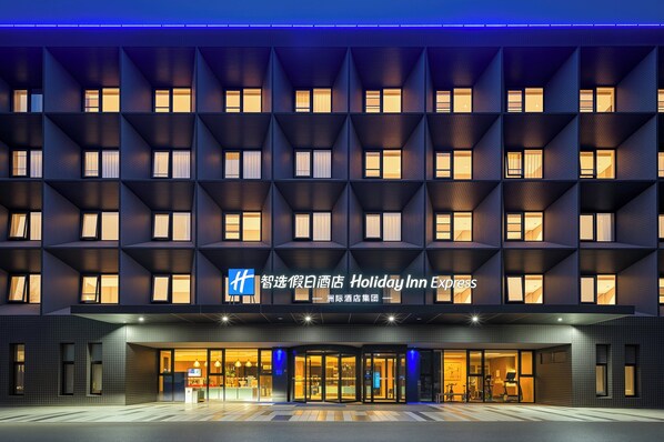 Un hotel Holiday Inn Express con fachada moderna, varios balcones y una entrada bien iluminada.