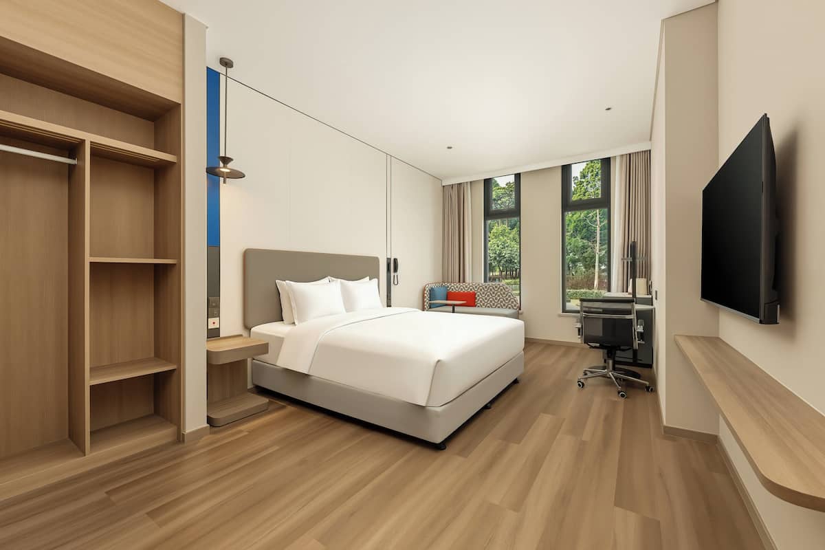 Ein modernes Hotelzimmer mit Bett, Schreibtisch, Stuhl, Fernseher und Kleiderschrank.