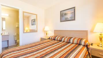 A hotel room with a large bed, a bedside table with a lamp, a nightstand, a mirror, and a painting on the wall.