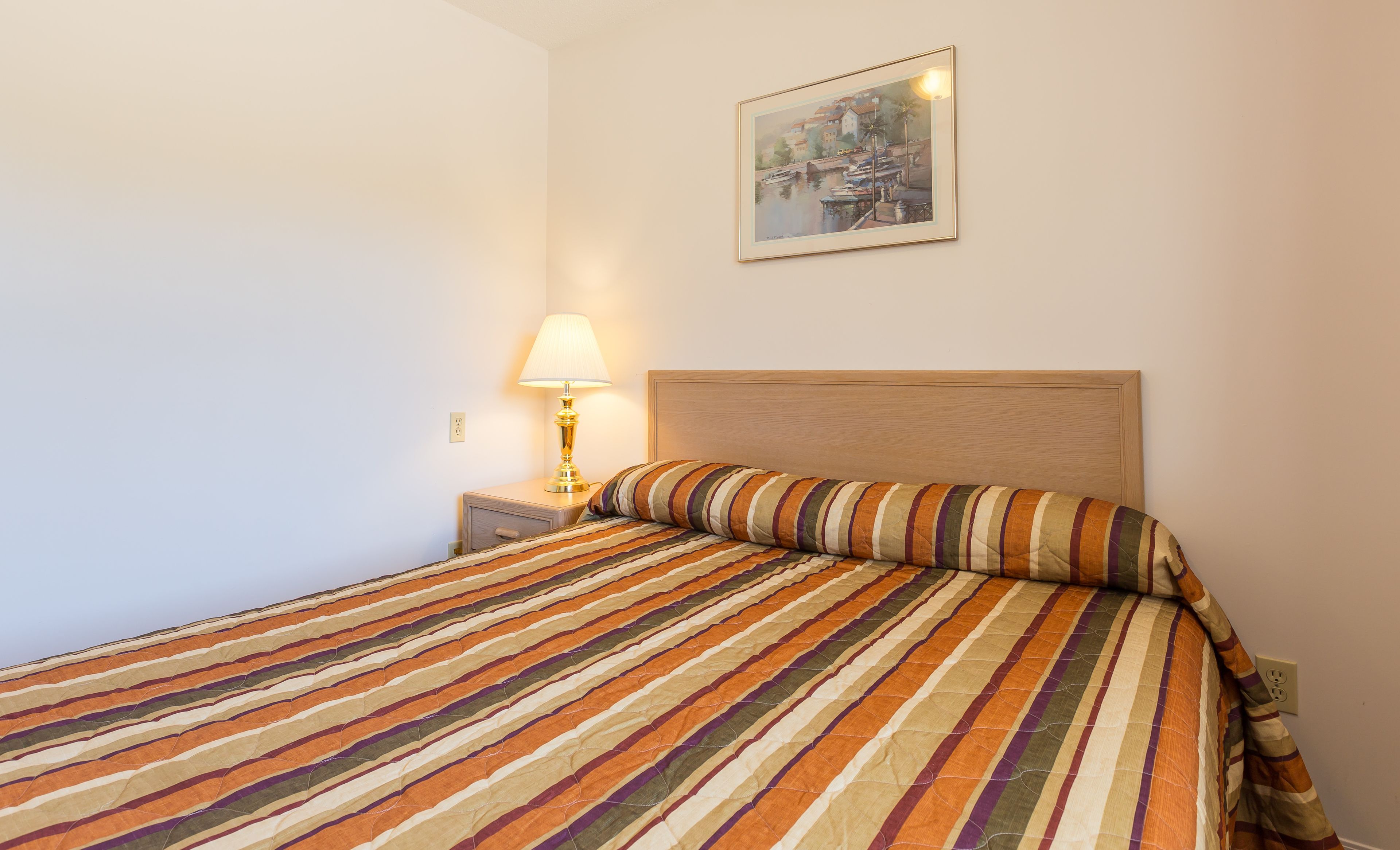 A hotel room with a bed, a nightstand, a lamp, and a painting on the wall.