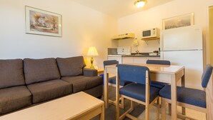 Un espacio habitable compacto con un sofá, una pequeña mesa de comedor y sillas. Se ve una cocina al fondo, con microondas, cocina y refrigerador.