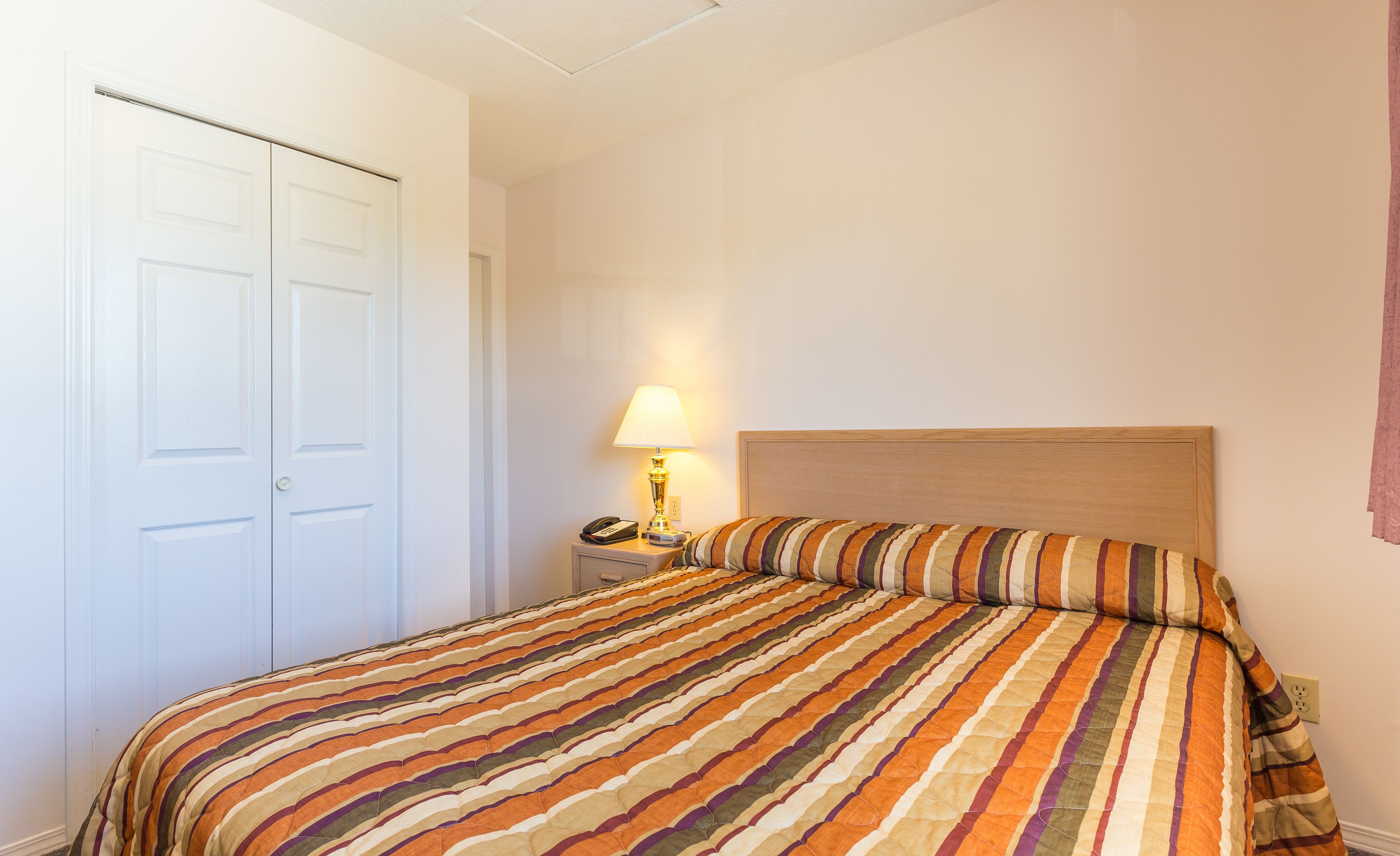 Ein Schlafzimmer mit Bett, Nachttisch, Lampe und Tür.