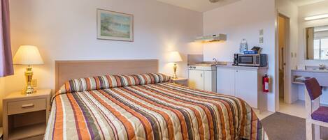 A hotel room with a large bed, a desk, a microwave, and a small kitchenette.