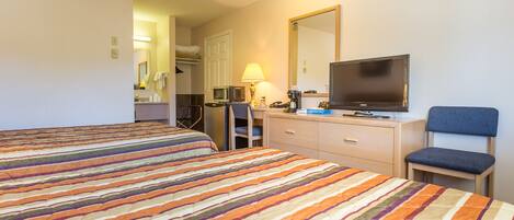 A hotel room with two beds, a desk with a computer, a chair, a television, and a mirror.