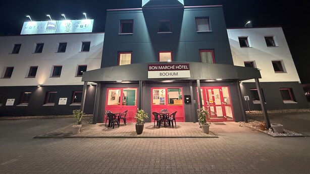 Et hotel med et tydeligt skilt, en overdækket indgang og udendørs siddepladser.