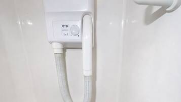 A white bathroom with a wall-mounted hair dryer and a white shelf.