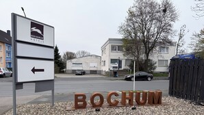 Et skilt for 'Bon Marche Hotels' med en pil, der peger mod venstre, og ordet 'BOCHUM' i store bogstaver på jorden.