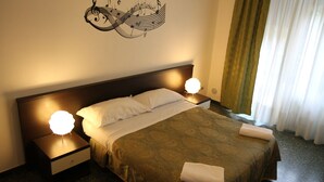 Habitación de hotel con cama, dos lámparas de noche, un cuadro musical en la pared y una ventana con cortinas.