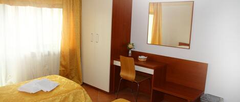 A hotel room with two beds, a desk, a chair, a wardrobe, a mirror, and a trash bin.
