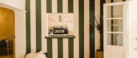 A room with a striped wall, a coffee machine, a door, and a sheep.