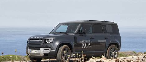 Un SUV negro estacionado en terreno rocoso con vista al mar.